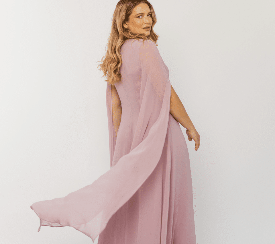 Wizualizacja kobiety w długiej, lejącej się sukni wieczorowej w kolorze pudrowego różu, z peleryną z szyfonu